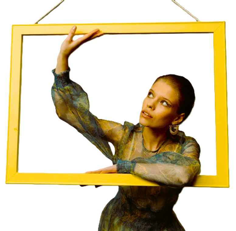 Woman wearing patterned sheer top posing inside a large yellow picture frame on a white background